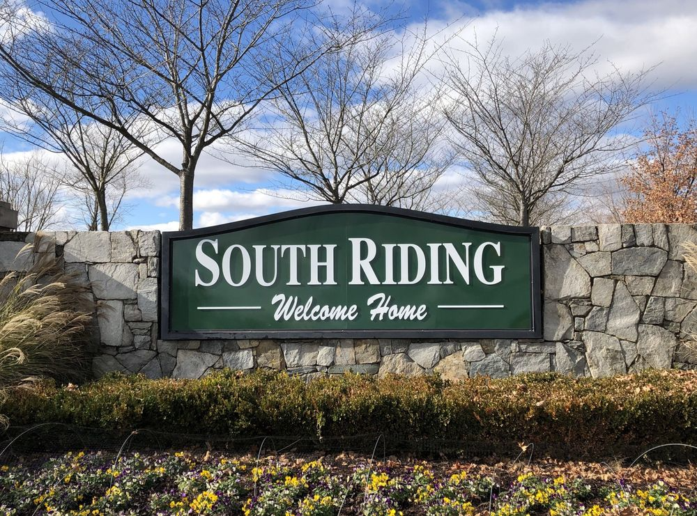 South Riding entrance sign on a stone wall with trees and flowers in the background