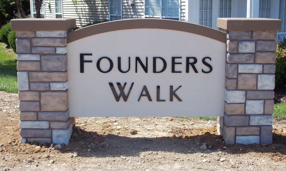 Stone and beige sign reading “Founders Walk” on a landscaped path entrance