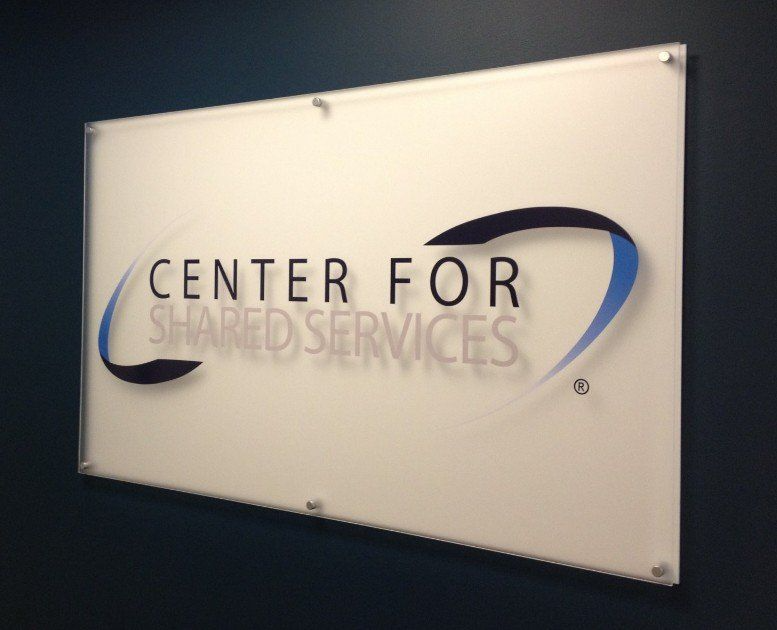 Wall sign reading “Center for Shared Services” in black and blue on a white background.
