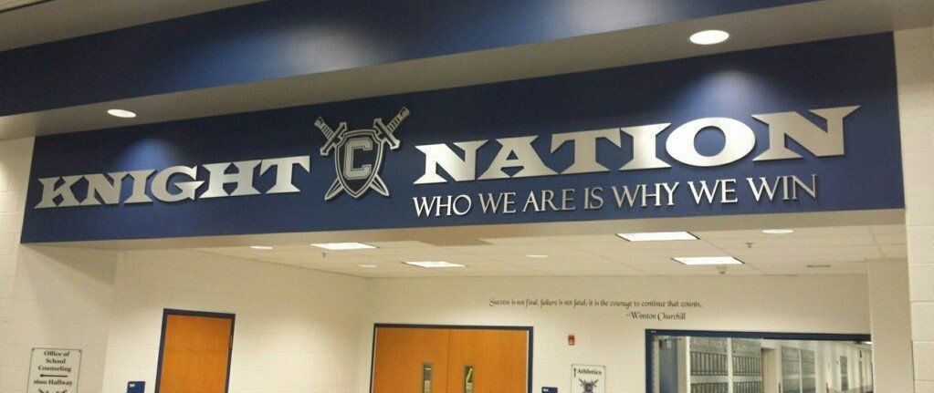 “Knight Nation” school banner in blue and white above wooden doors inside a building