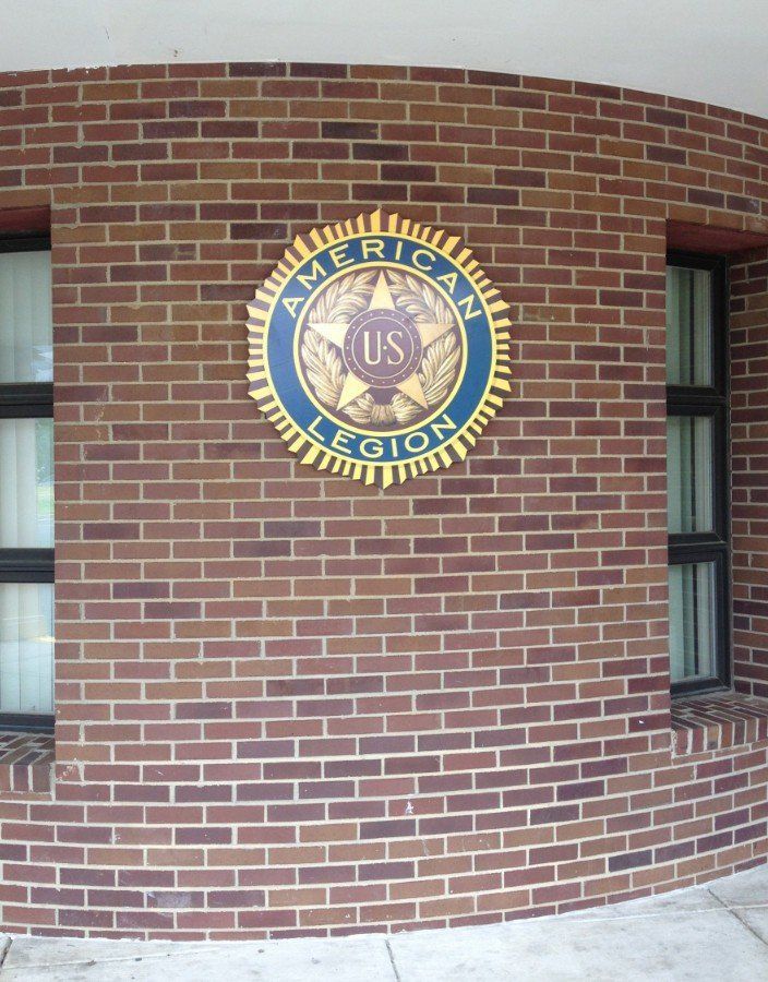 Circular U.S. Army Medical Command emblem on a brick building wall, beside windows and a doorway.