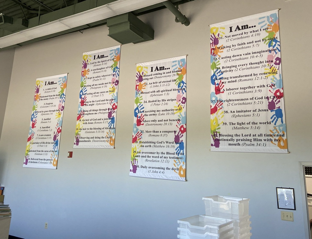 Colorful classroom posters with large title headings hang on a wall above stacked plastic trays.