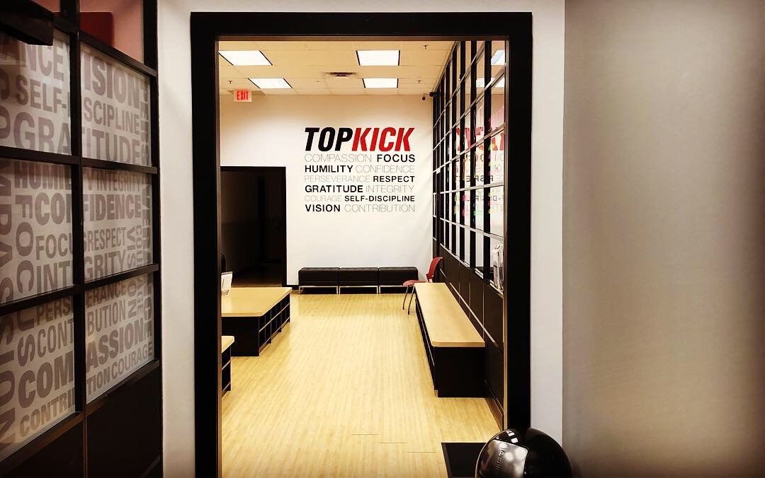 Modern office hallway opening into a small room with benches and a “TOPKICK” wall sign.