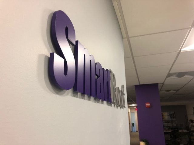 Purple “Smarts…” wall sign in an office hallway with white walls and ceiling tiles