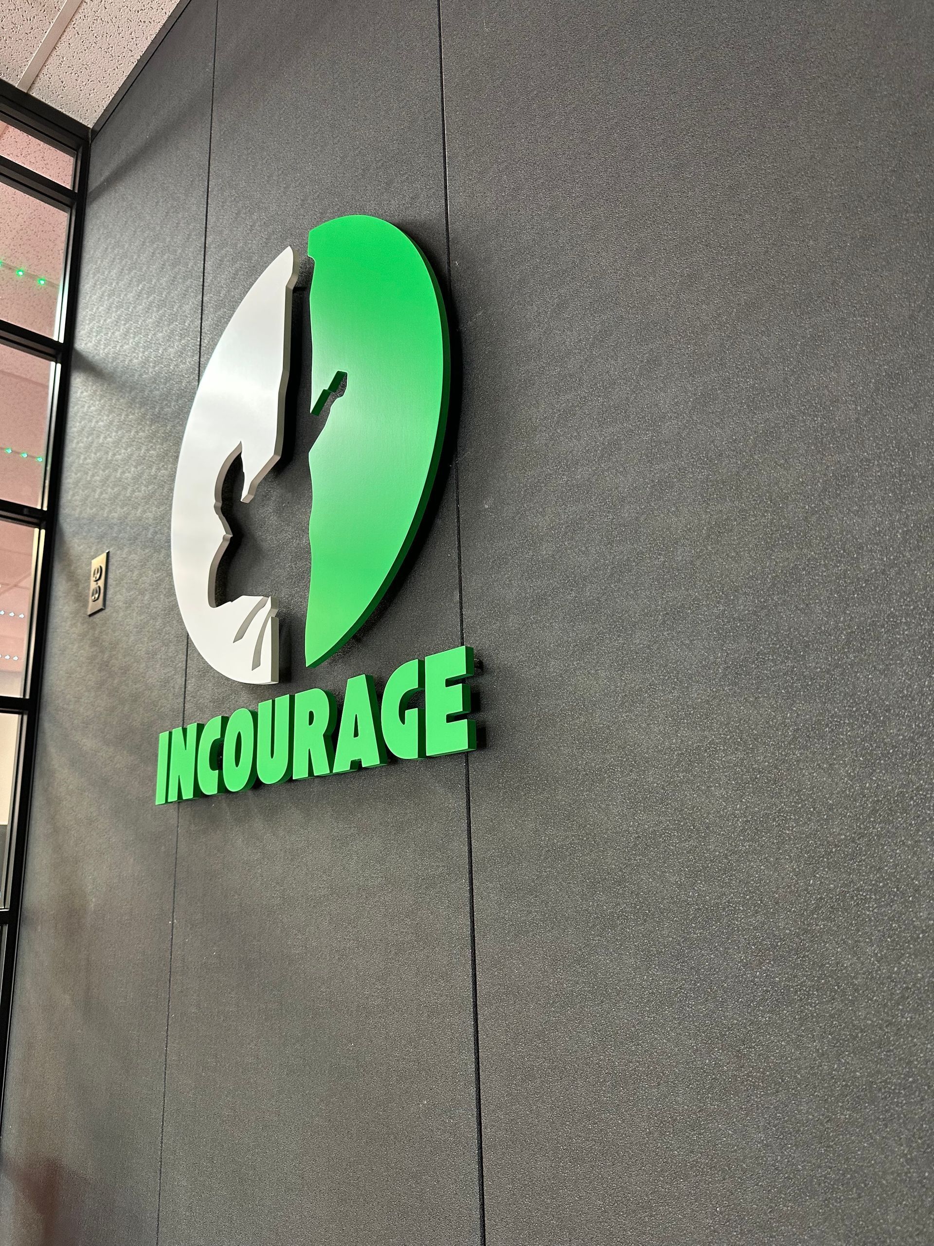 Green and white McQurage logo sign on a gray wall corner