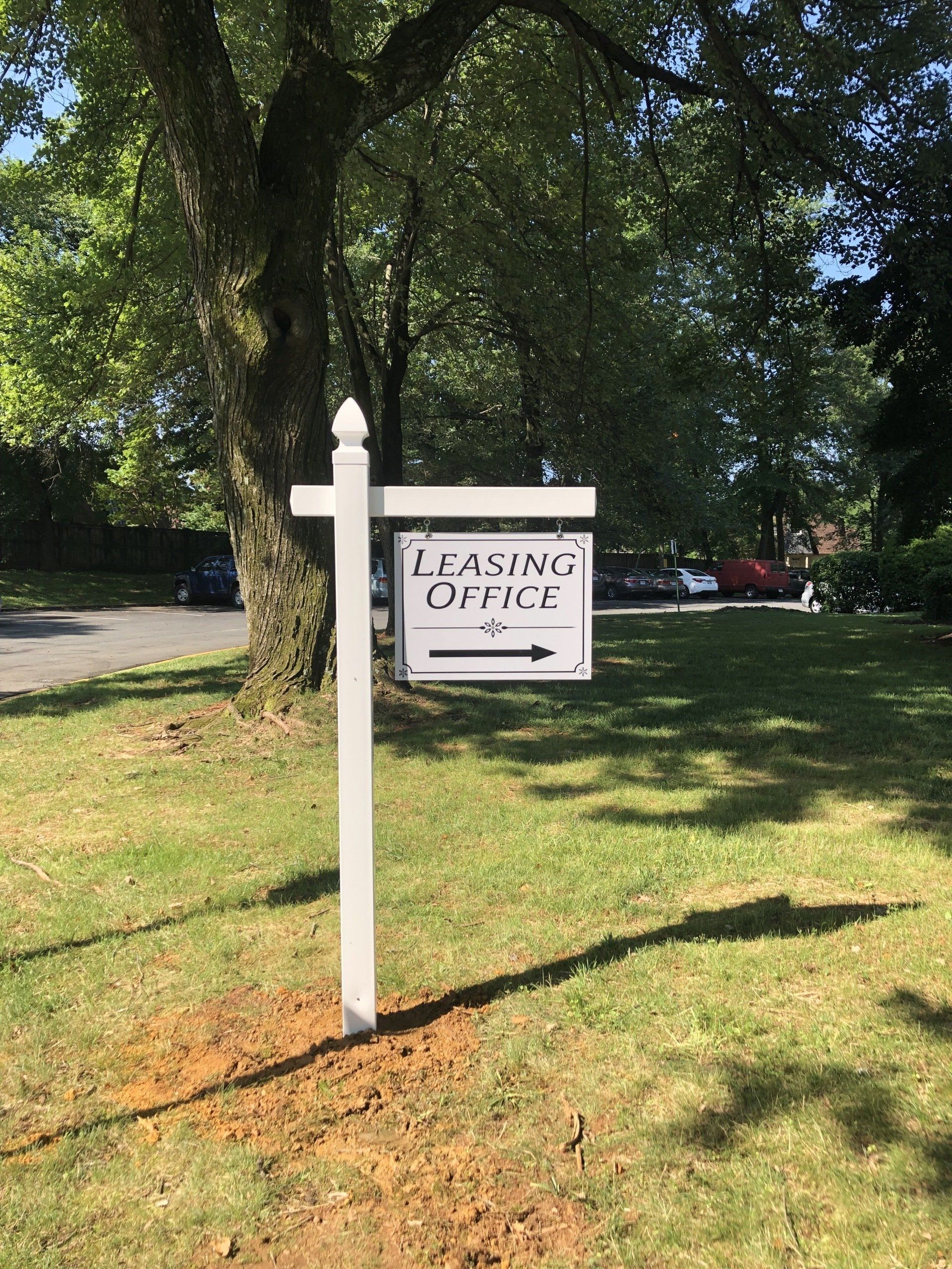 White signpost reading “T. L. Aiming Open” on a grassy lawn under trees, with parking lot in background