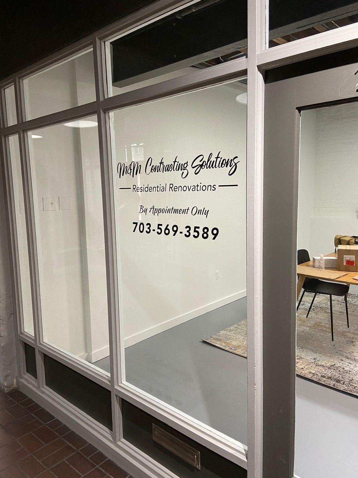 Glass storefront with white interior wall and business sign, viewed from outside.