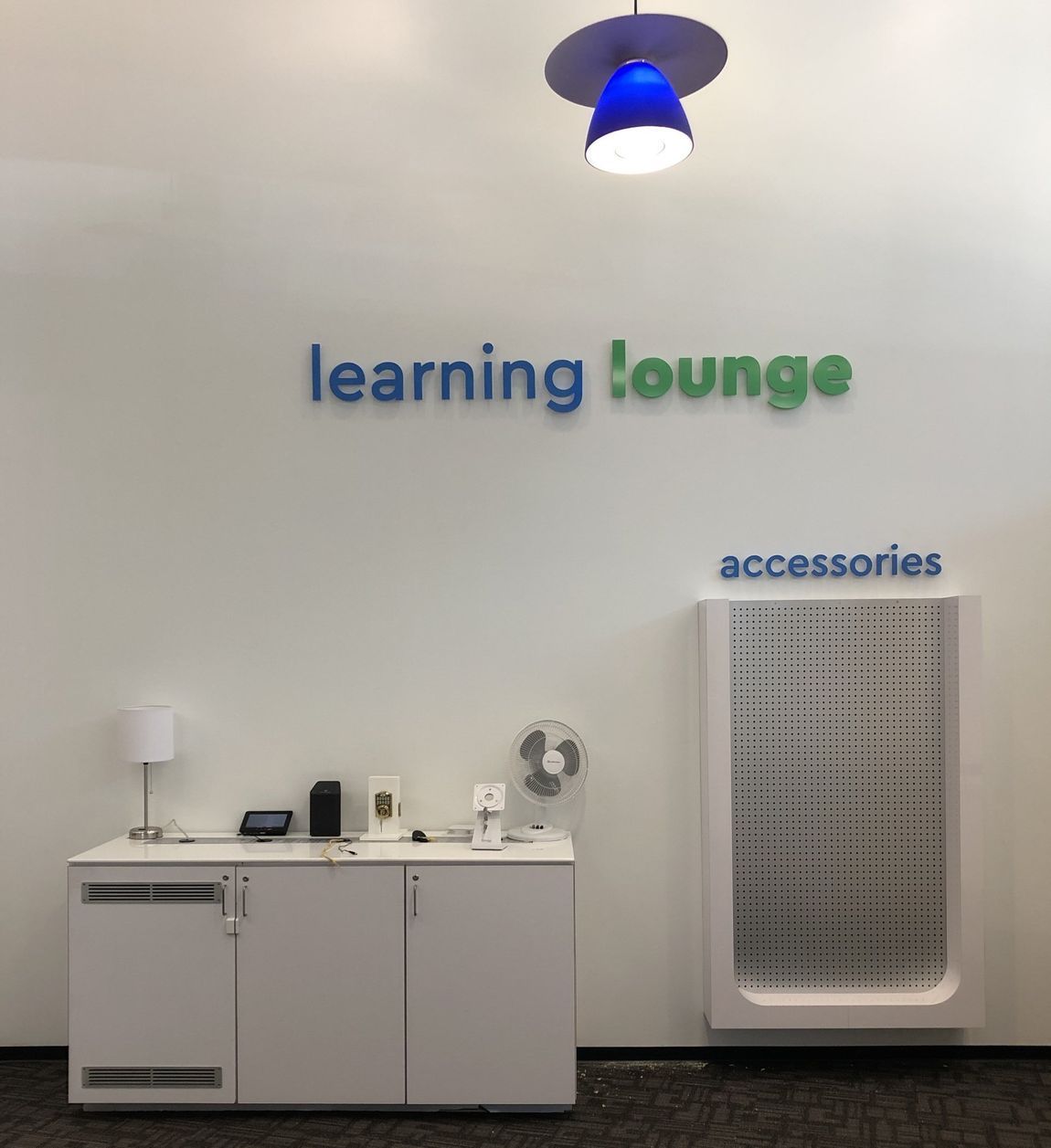 Learning lounge wall with blue and green sign, white cabinet, and accessories shelf under a blue light