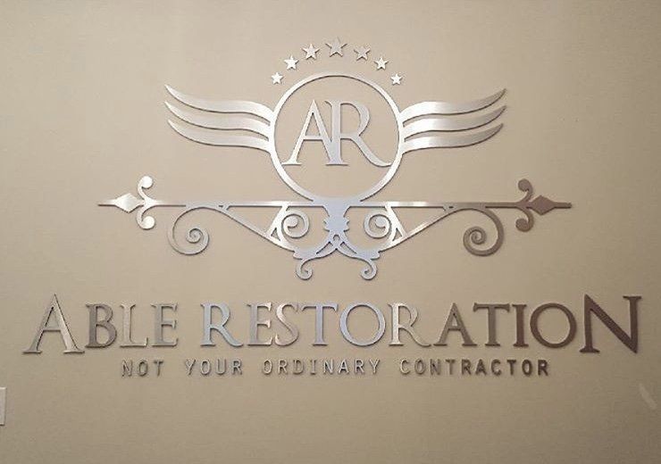 Metal wall sign for Able Restoration with AR monogram and slogan “Not Your Ordinary Contractor”