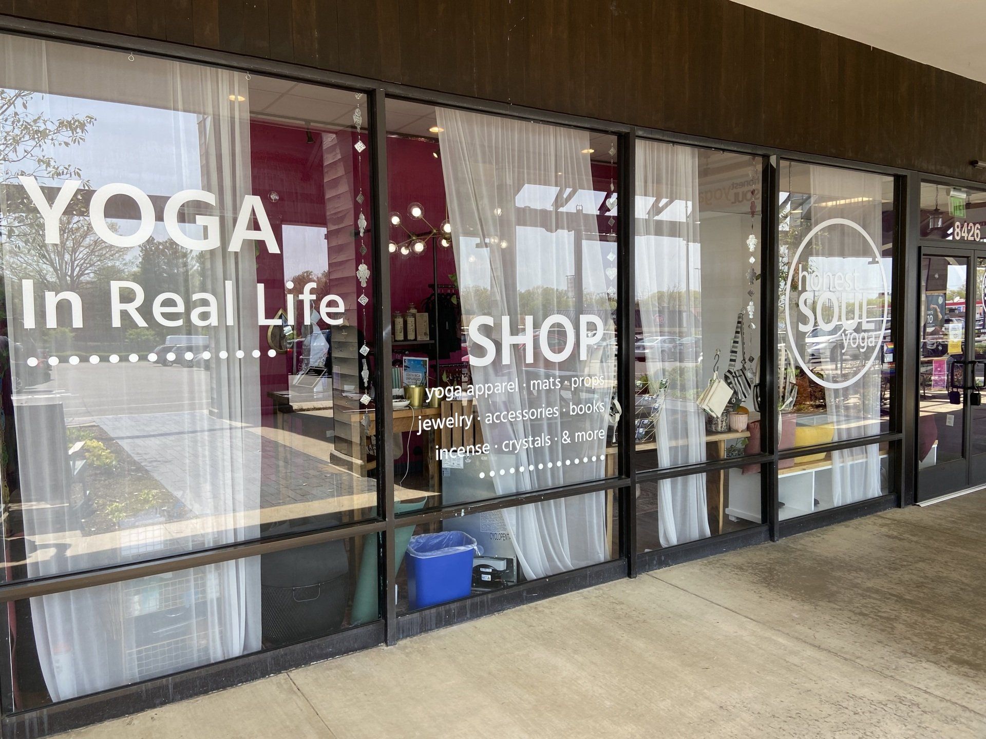 Storefront windows with large “YOGA In Real Life” and “SHOP” signs, seen from a walkway.