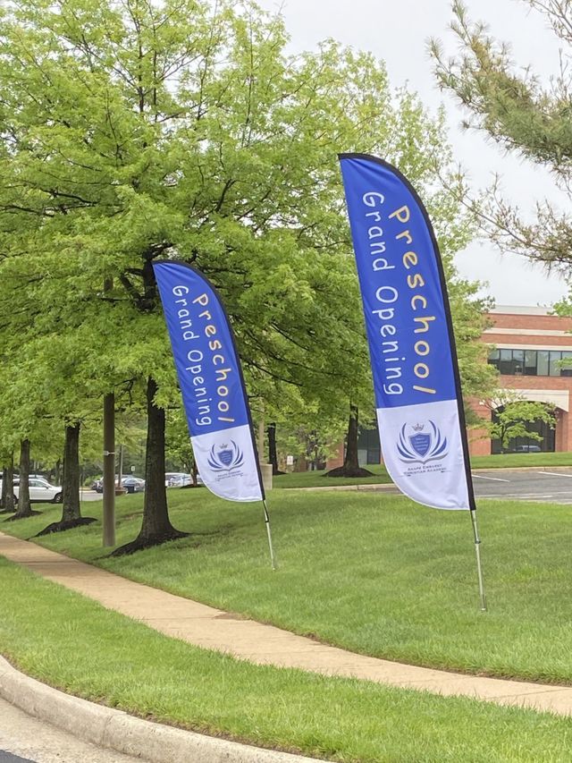 Blue “Freshman Arrival” banners along a grassy sidewalk near trees and a brick building