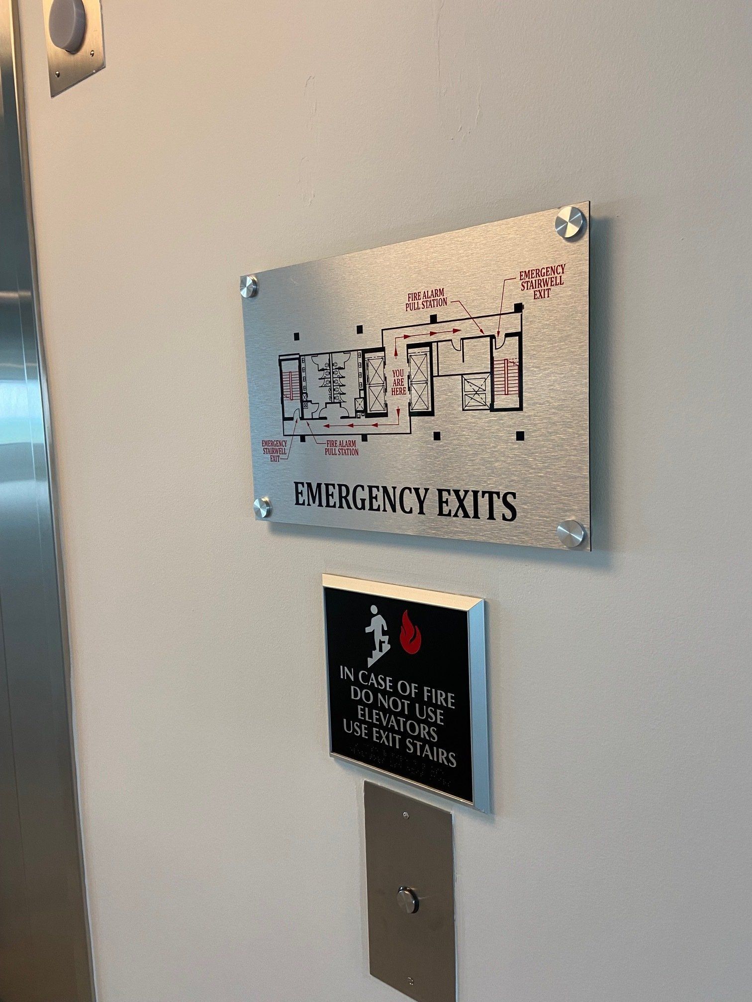 Wall signs showing an emergency exit floor map above a black safety notice on a beige wall