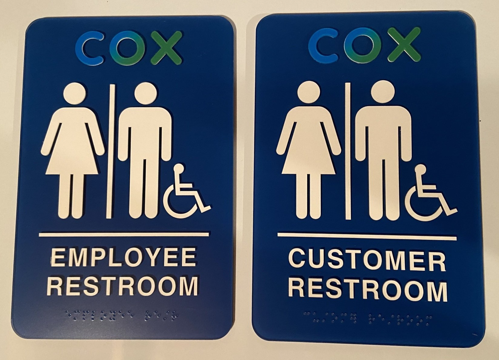 Two blue Cox restroom signs for employee and customer restrooms with universal icons.