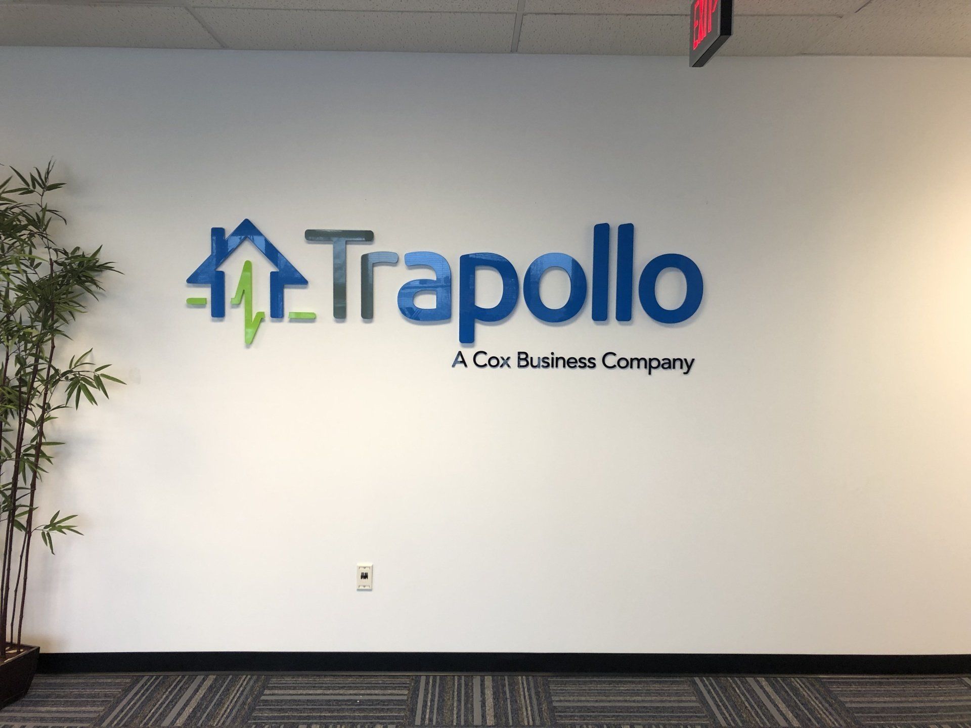 Trapollo office wall logo in blue and green with tagline, on a white hallway wall