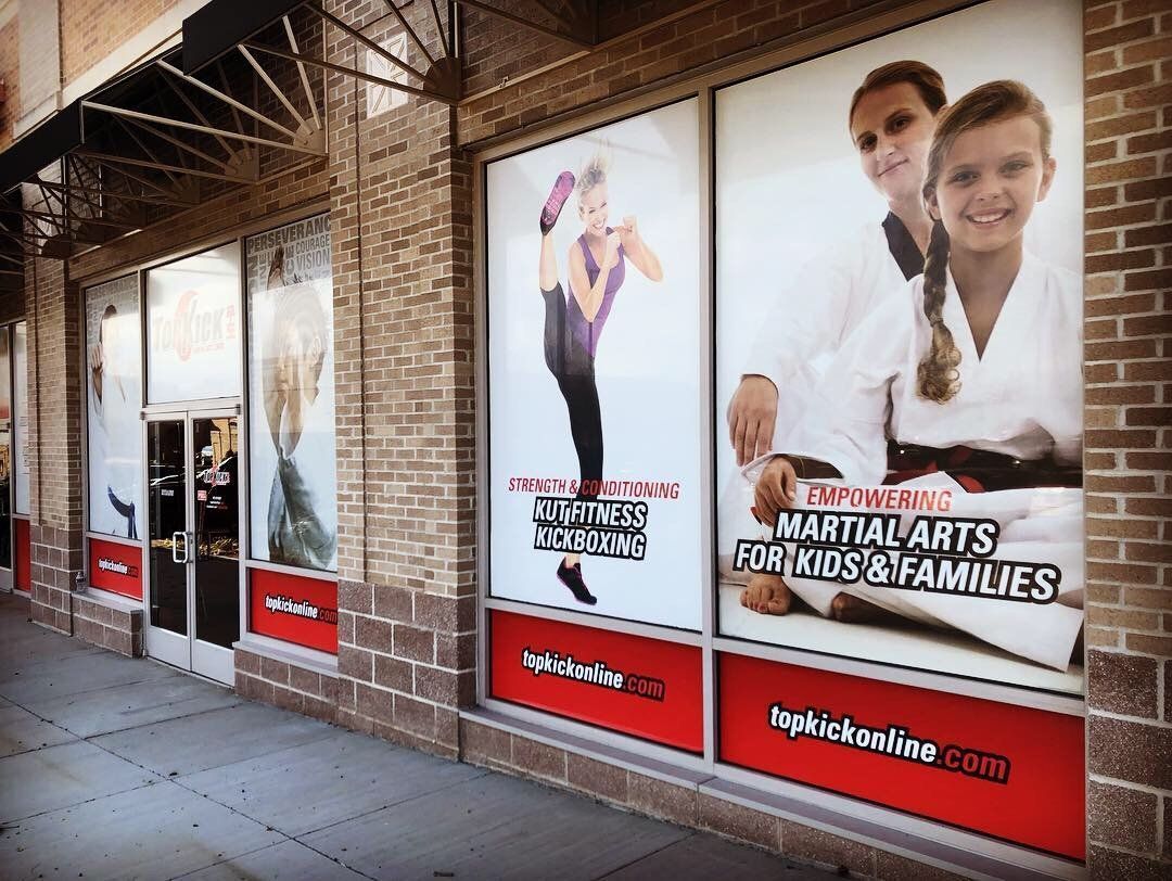 Storefront windows with large promotional posters and a red banner along a brick sidewalk
