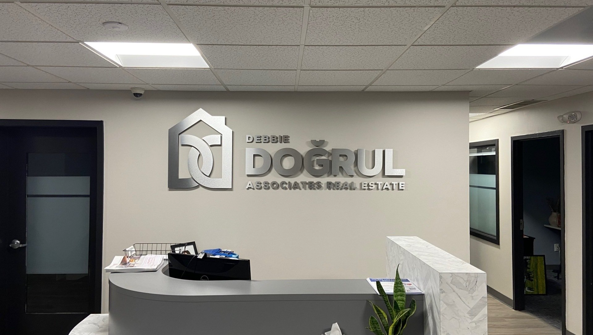 Office lobby with “DOGRUL” logo on the wall, reception desk, and open hallway doors