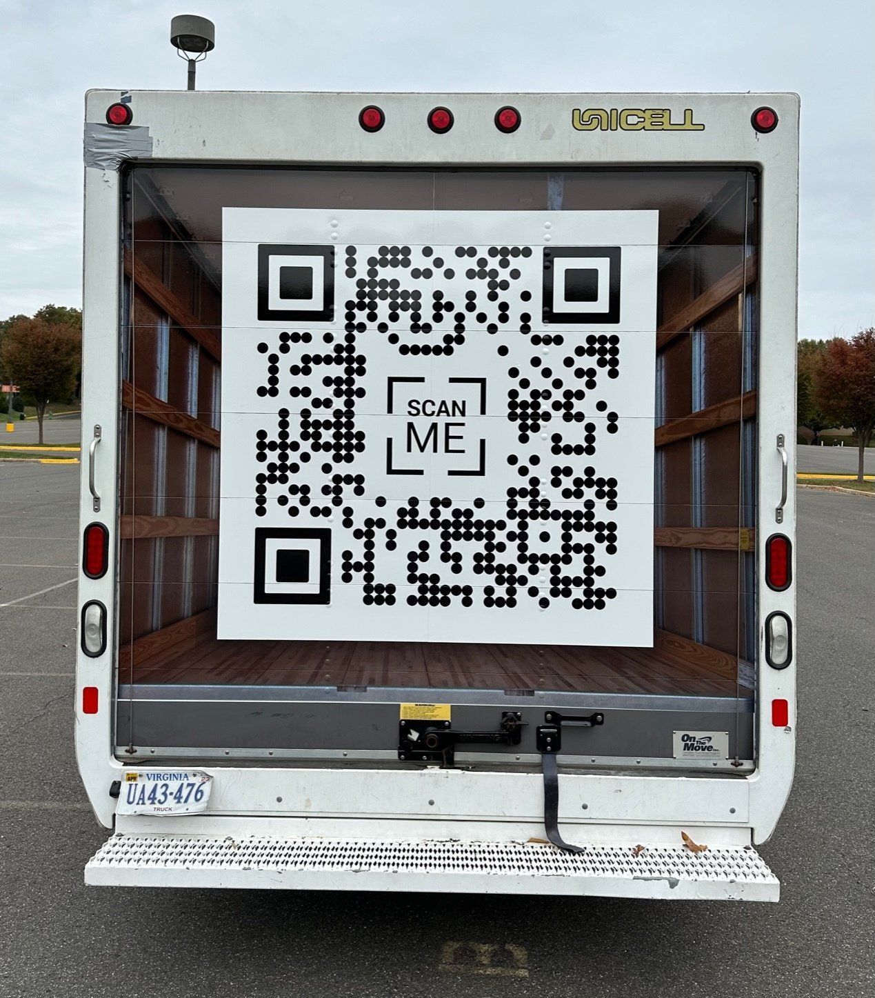 QR code sign on the back of a white truck, with “SCAN ME” in the center.