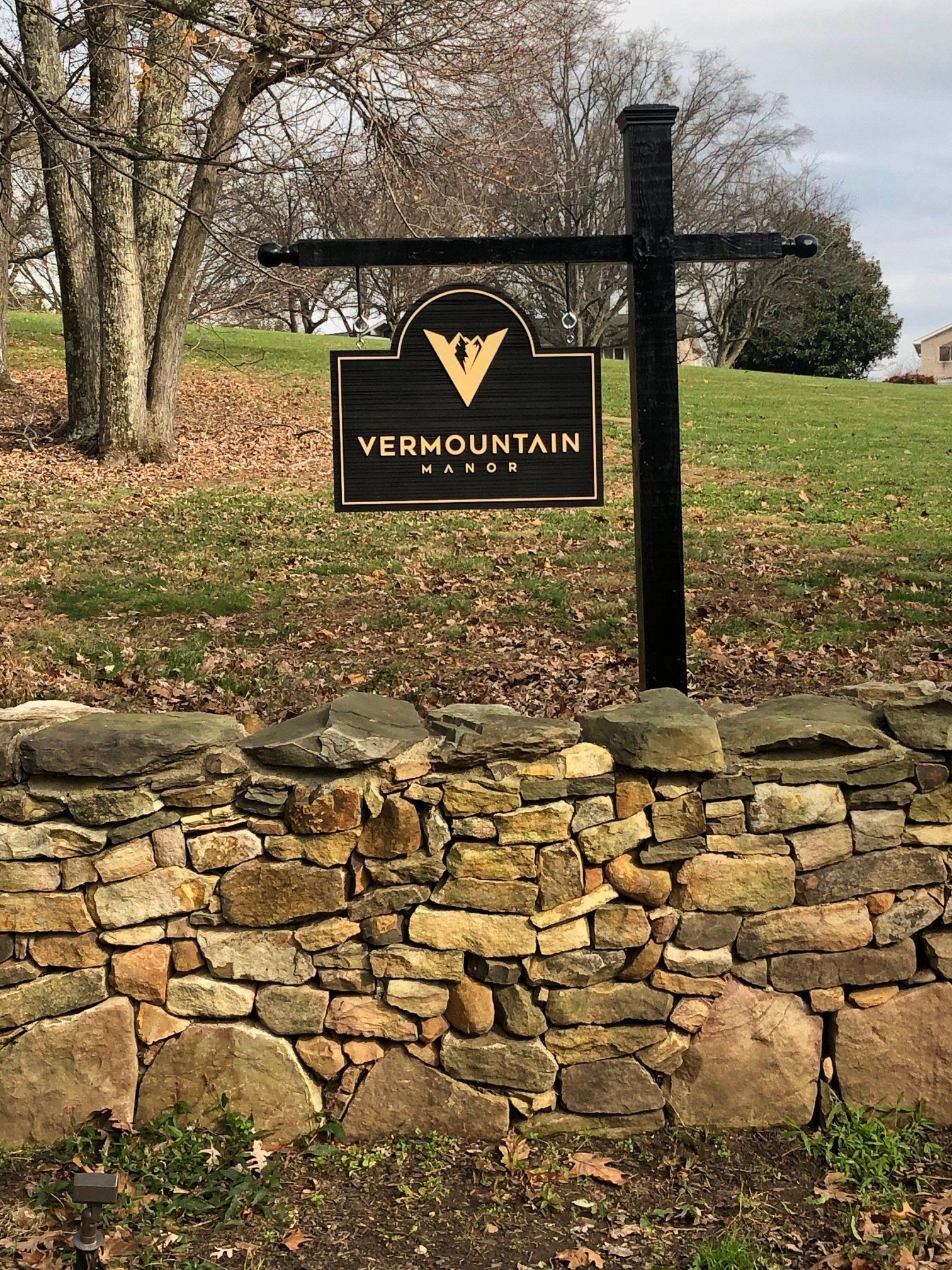 VerMounTain sign on black post above a stone wall in a grassy park setting