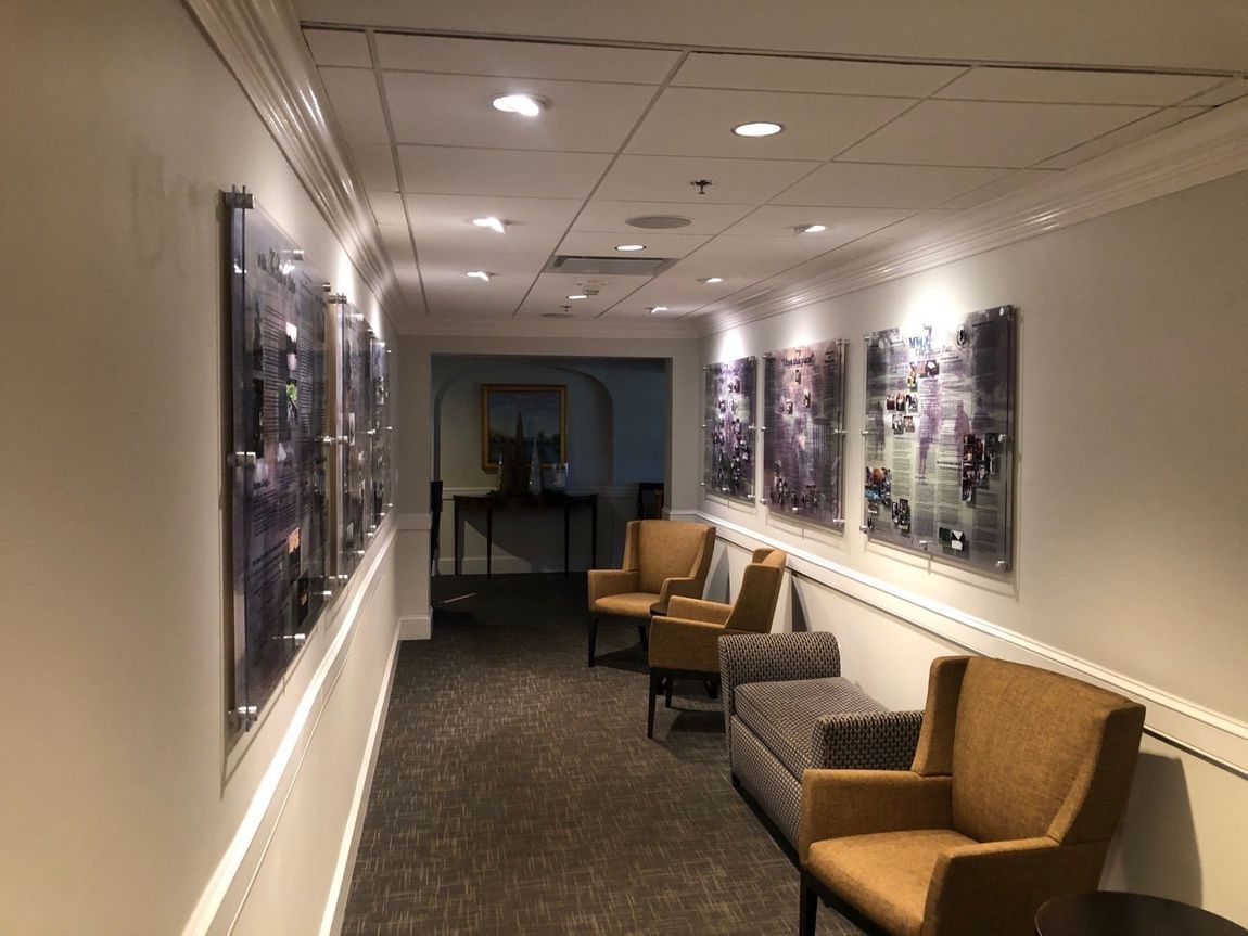 Modern hallway with framed artwork, recessed lighting, and upholstered chairs along the wall.
