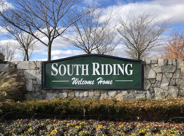 South Riding neighborhood entrance sign on a stone wall with trees and flowers under a blue sky