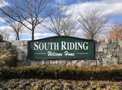 South Riding welcome sign on a stone wall with flowers and bare trees against a blue sky