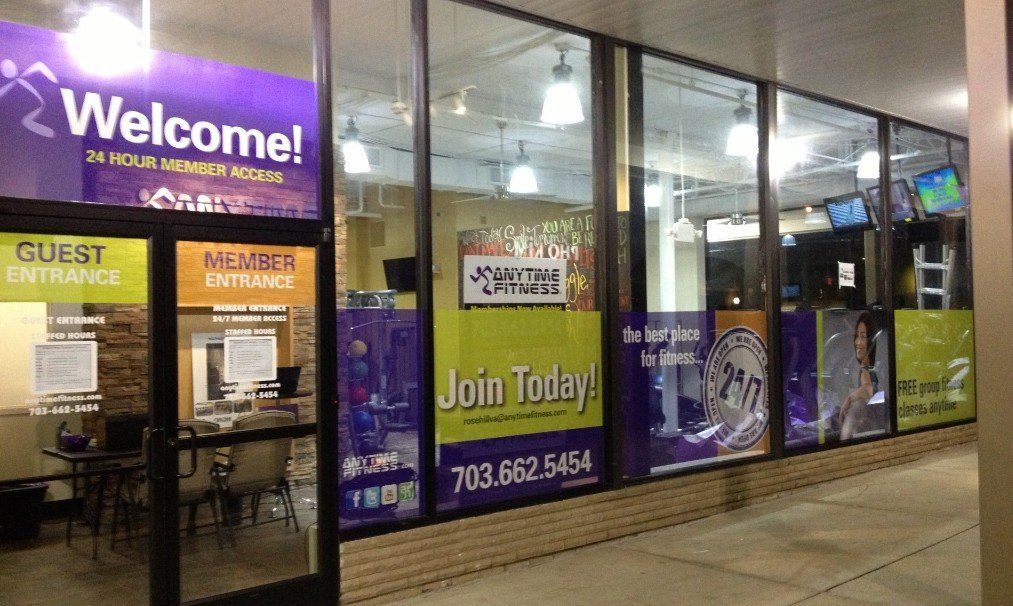 Glass storefront with “Welcome!” and “Join Today!” signs for a gym or fitness center at night