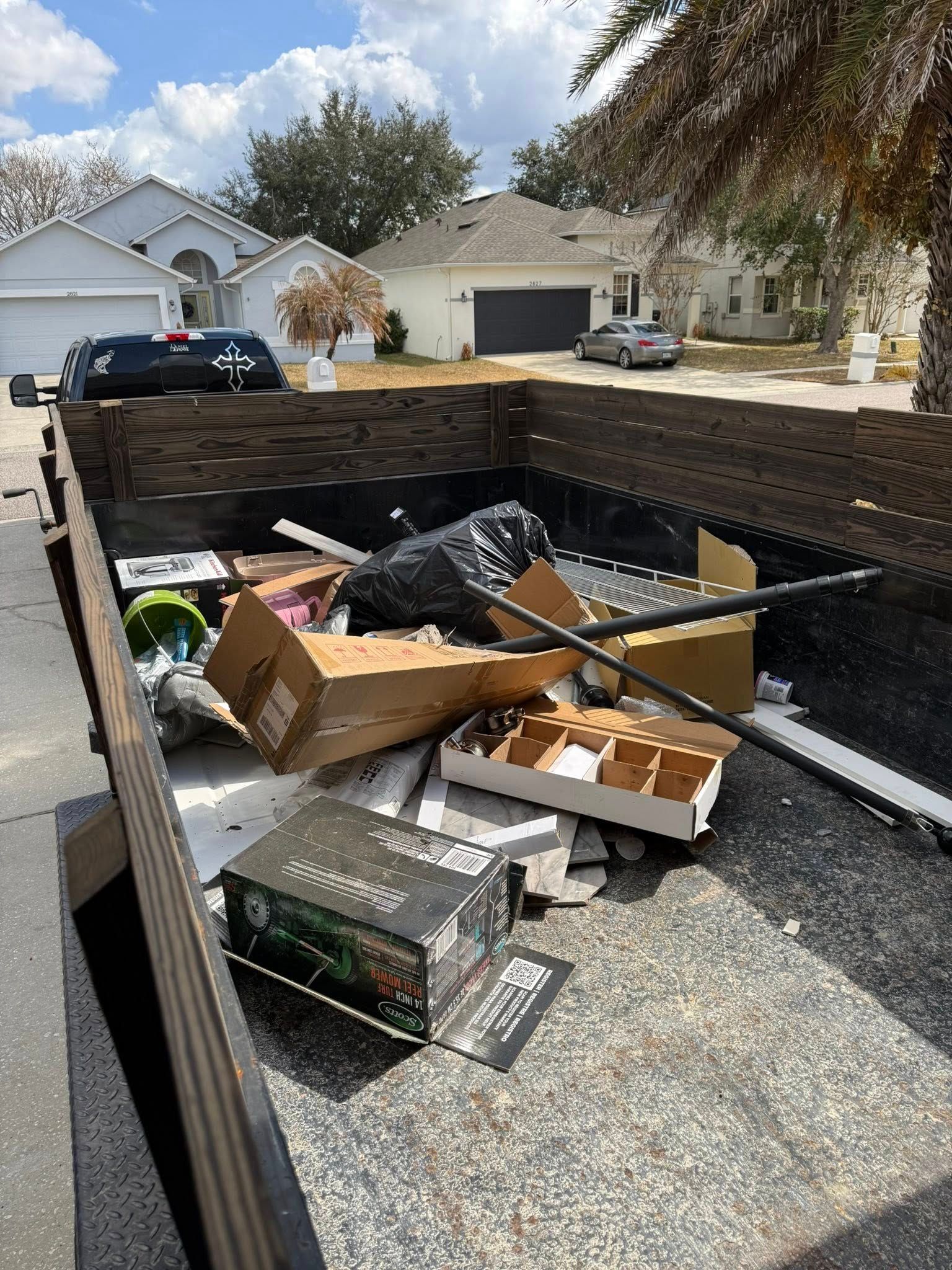 A large dumpster parked on a residential street containing scattered cardboard boxes and black trash bags.
