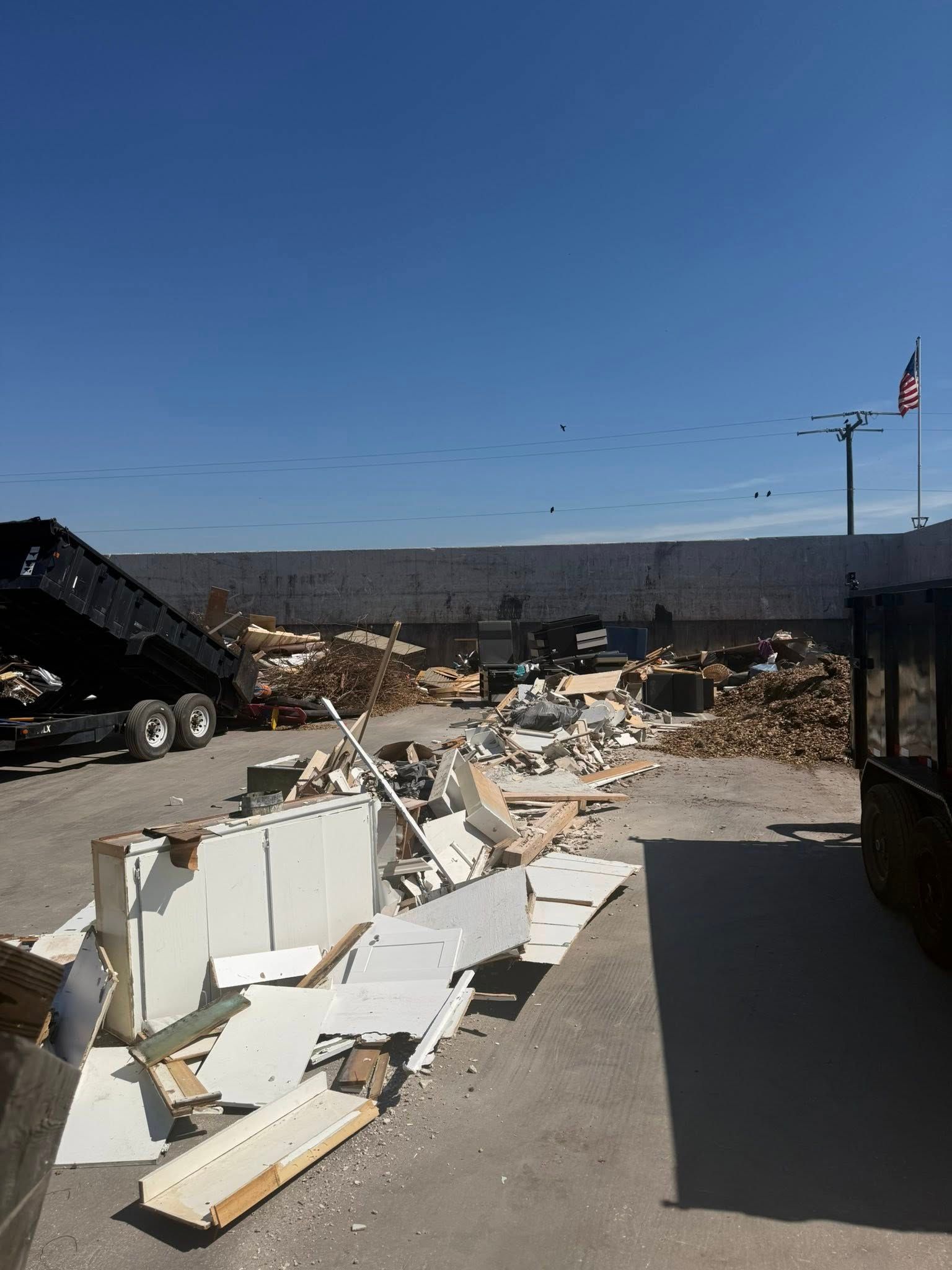 A dump truck parked on a gravel lot next to a large pile of debris and scrap construction materials under a clear sky.