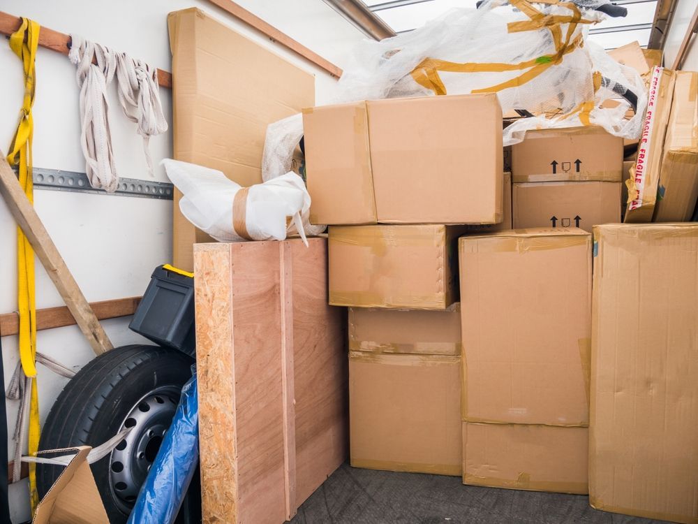 Moving truck interior packed with cardboard boxes, a spare tire, and wooden boards.