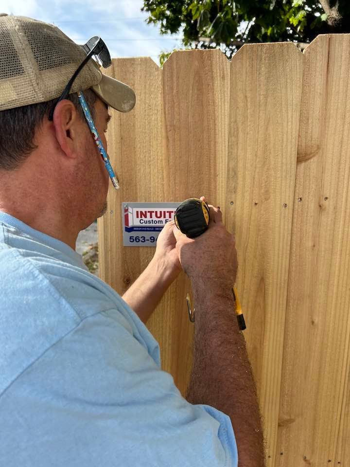 A man is measuring a wooden fence with a tape measure.