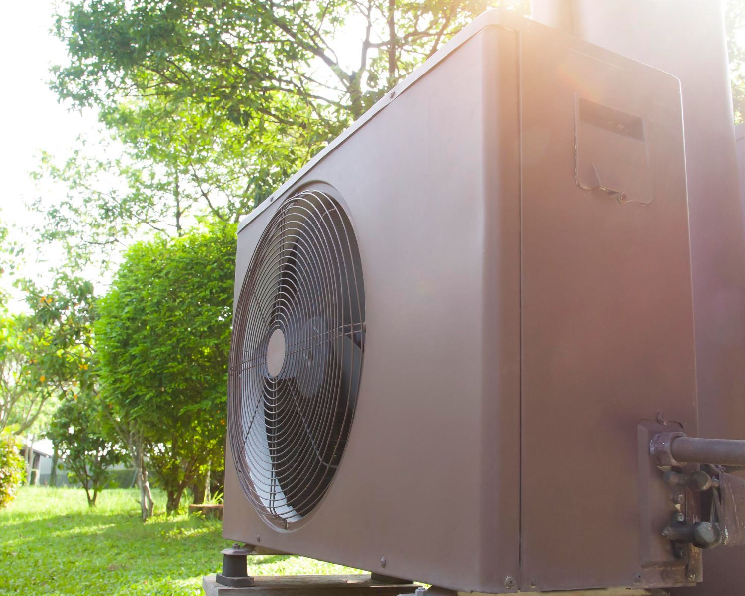 Brown HVAC unit outdoors with fan visible, set on a green lawn near trees.