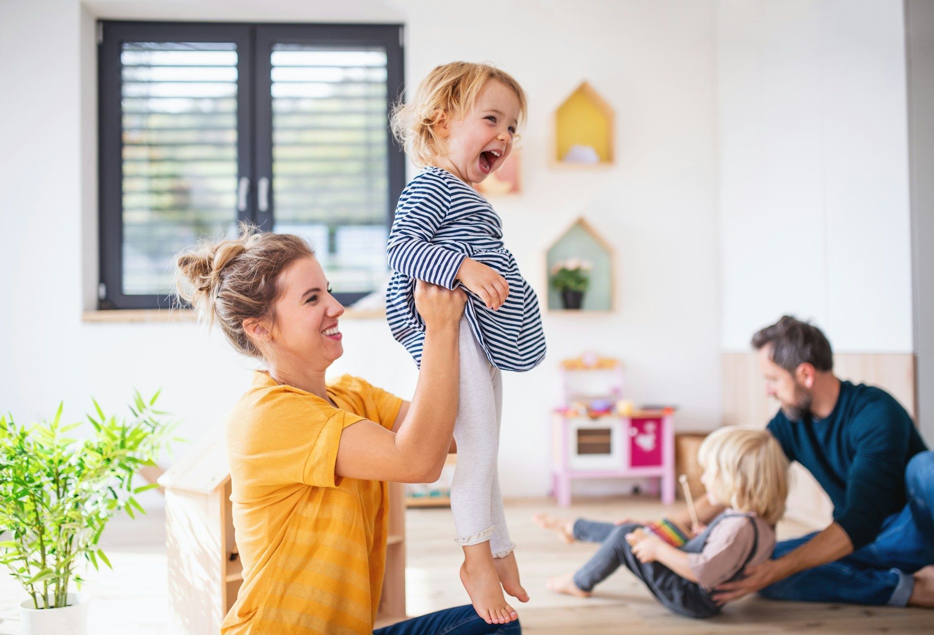 Family of three sitting on floor, interacting with a baby; near fireplace.