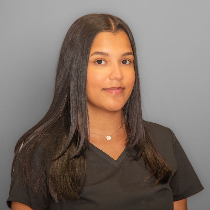 Portrait of a woman with long dark hair in a black V-neck shirt against a gray background