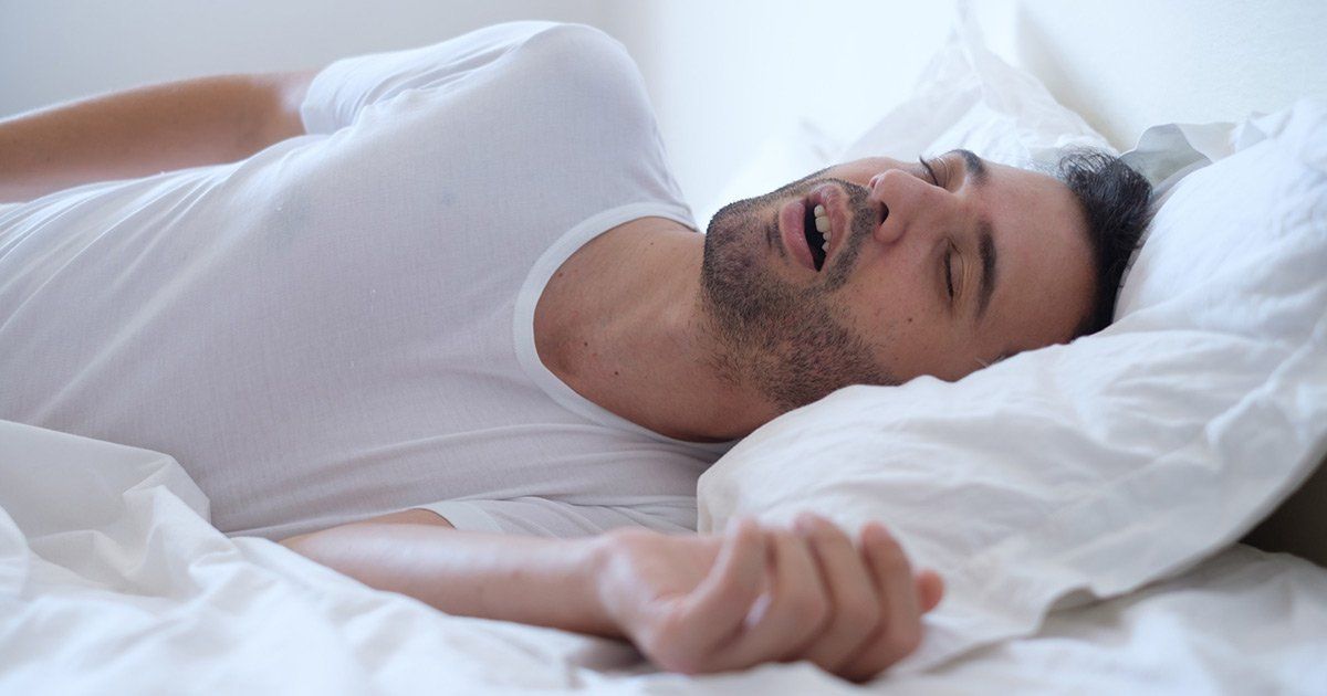 Man sleeping in bed, mouth open, on white sheets and pillow.