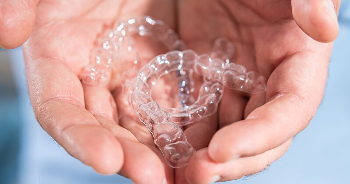 Hands holding clear aligners, likely for teeth straightening.