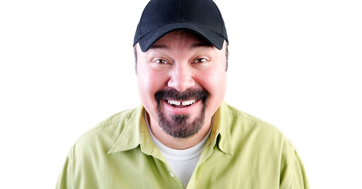 Man with black cap smiling, green shirt, white t-shirt, short dark beard, against a white background.