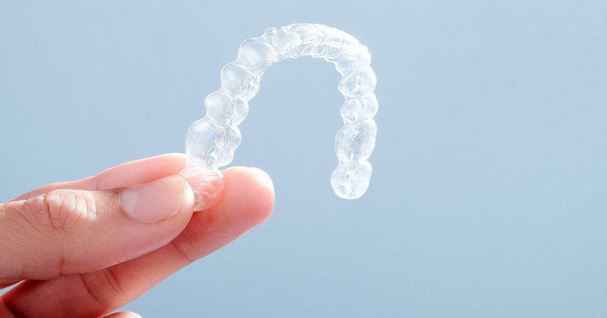 Clear Invisalign aligner held by a hand against a light blue background.