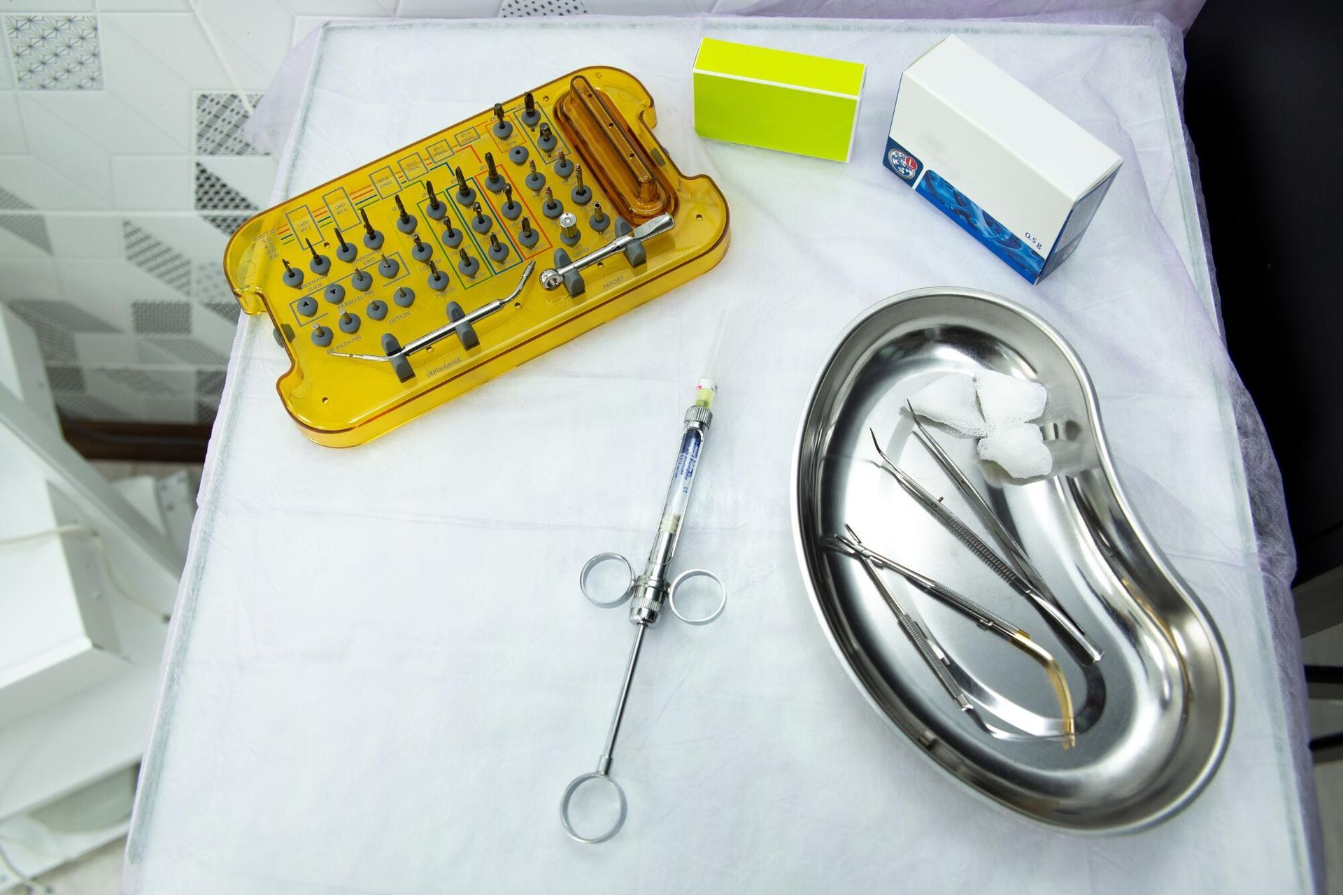 Dental tools on a white tray, including a yellow instrument case and stainless steel basin.