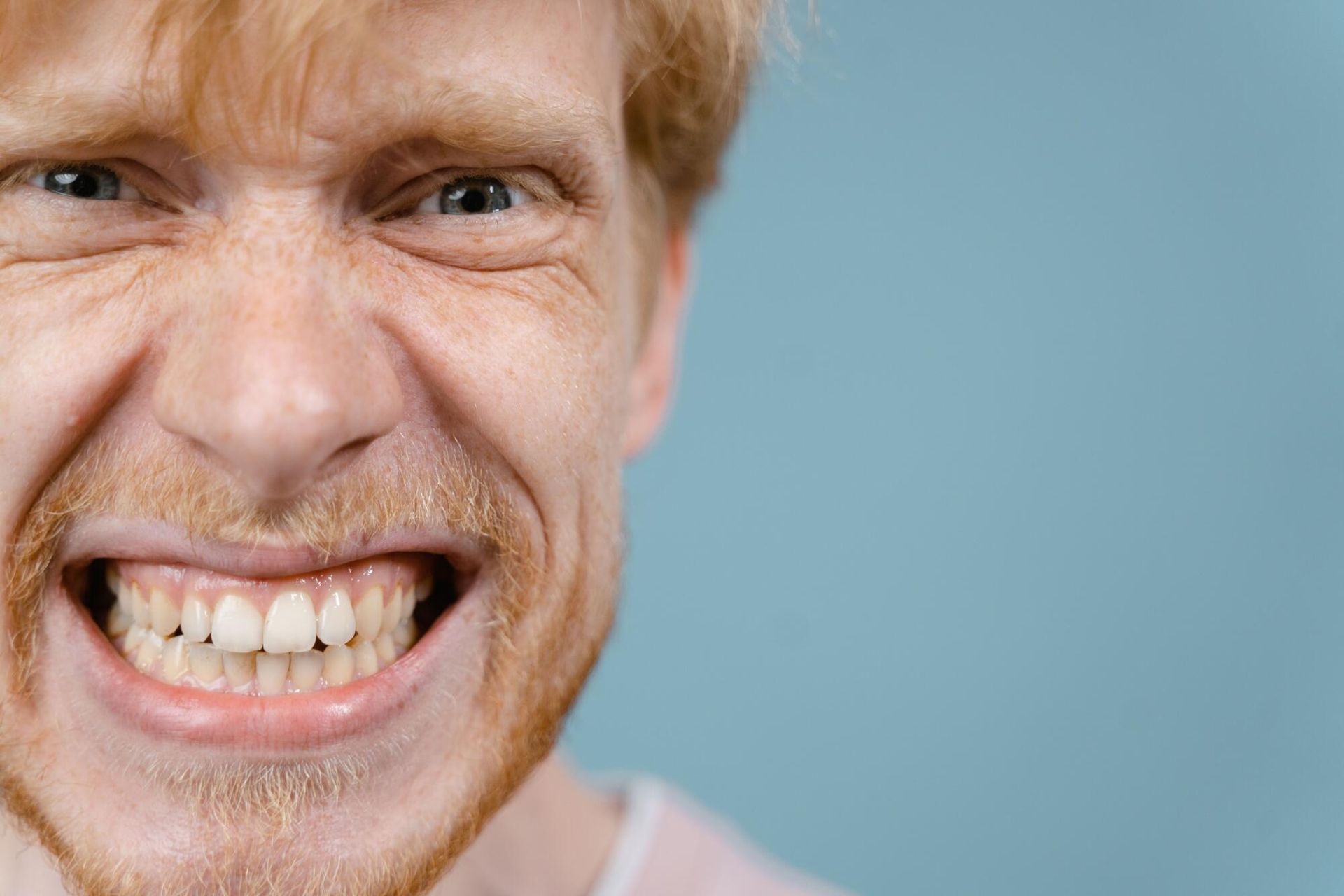 Close-up of a man grinning broadly, showing his teeth against a blue background
