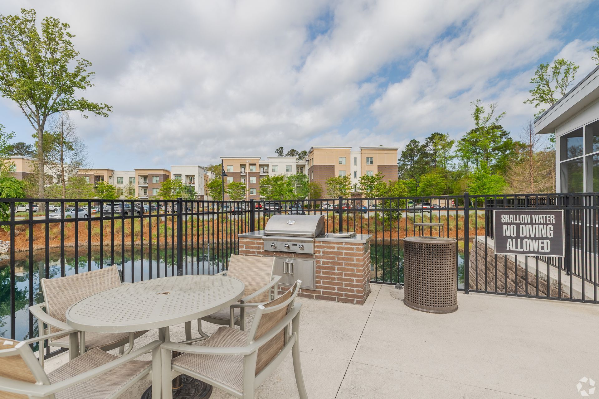 Patio seating area with round table, chairs, grill, and fire pit beside apartment buildings and pool area