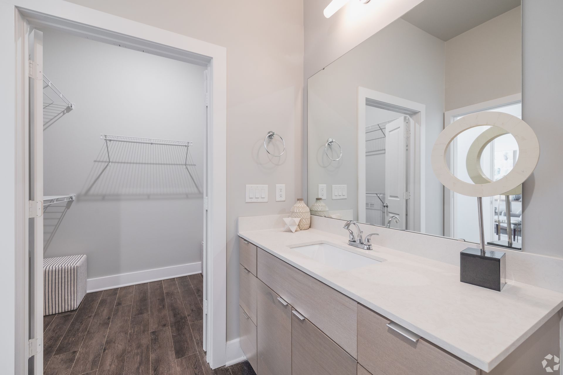 Bright bathroom vanity beside open closet with wire shelving and wood floor.