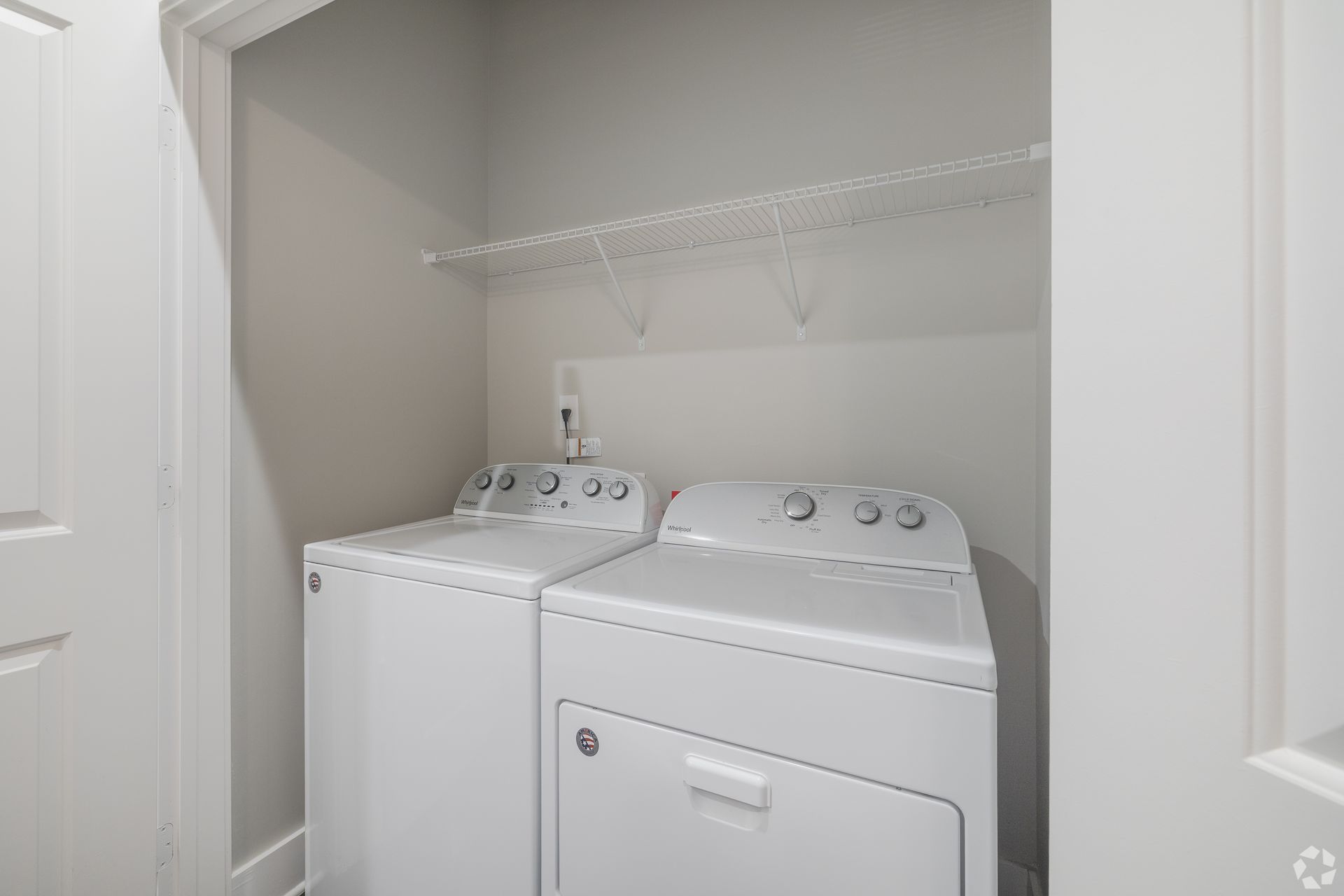 Small laundry closet with a washer and dryer beneath a white wire shelf.