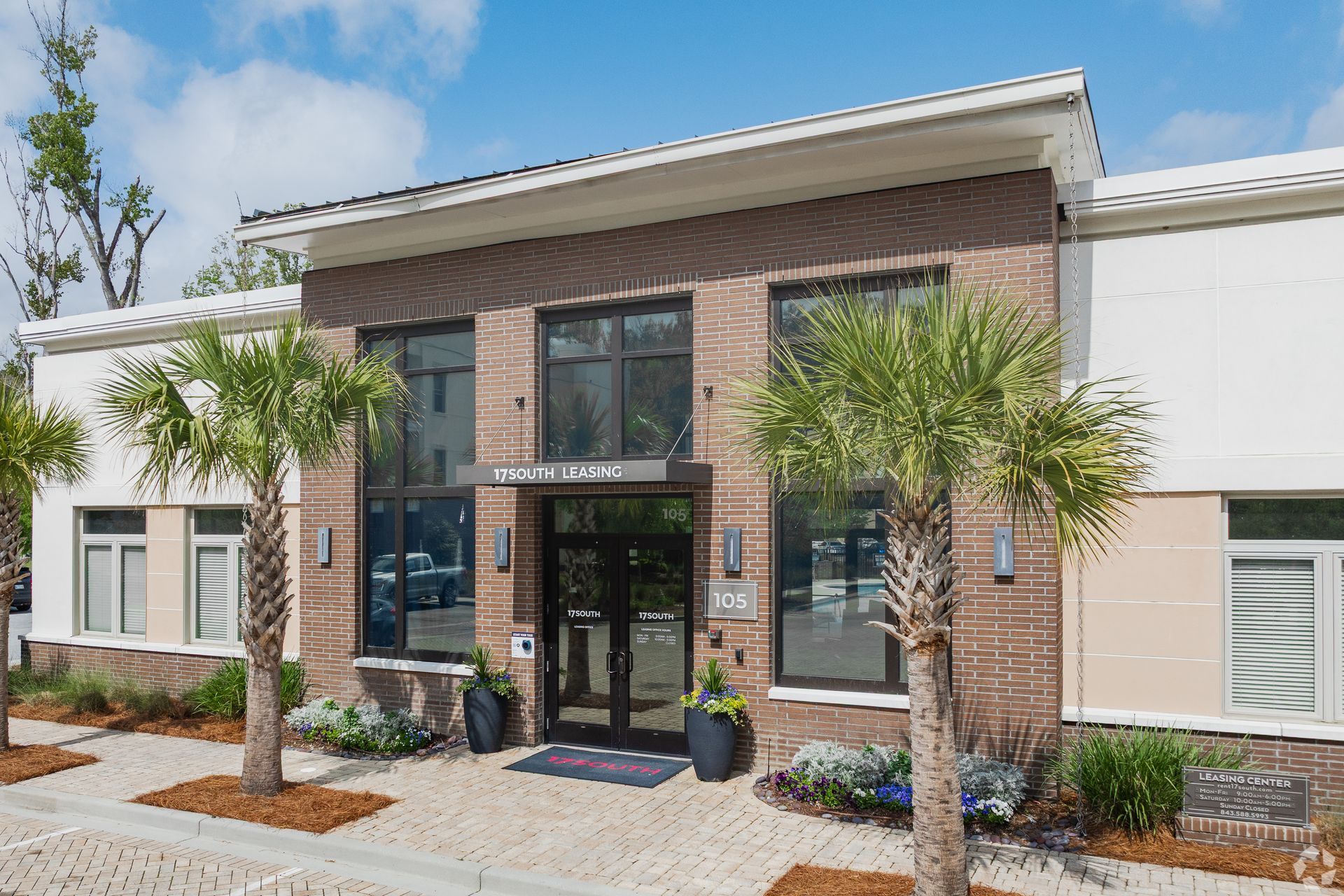 Modern brick office building entrance with glass doors, palm trees, and landscaped walkway
