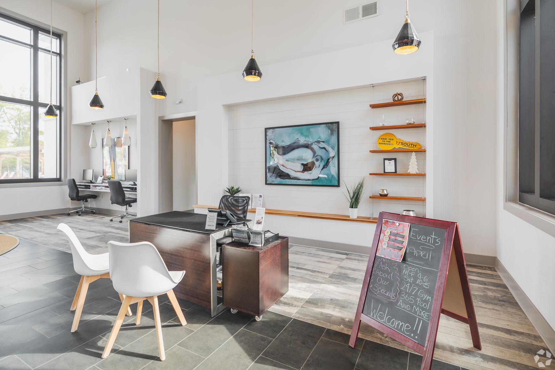 Bright modern café interior with tables, pendant lights, wall art, and a chalkboard sign near a window.