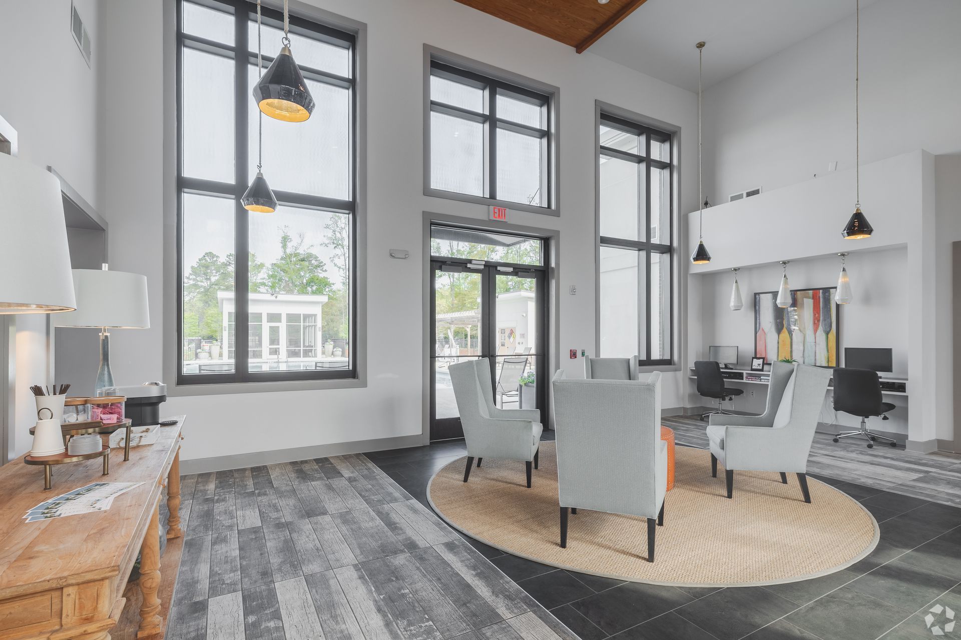 Modern open-concept living room with large windows, gray chairs, round rug, and fireplace.