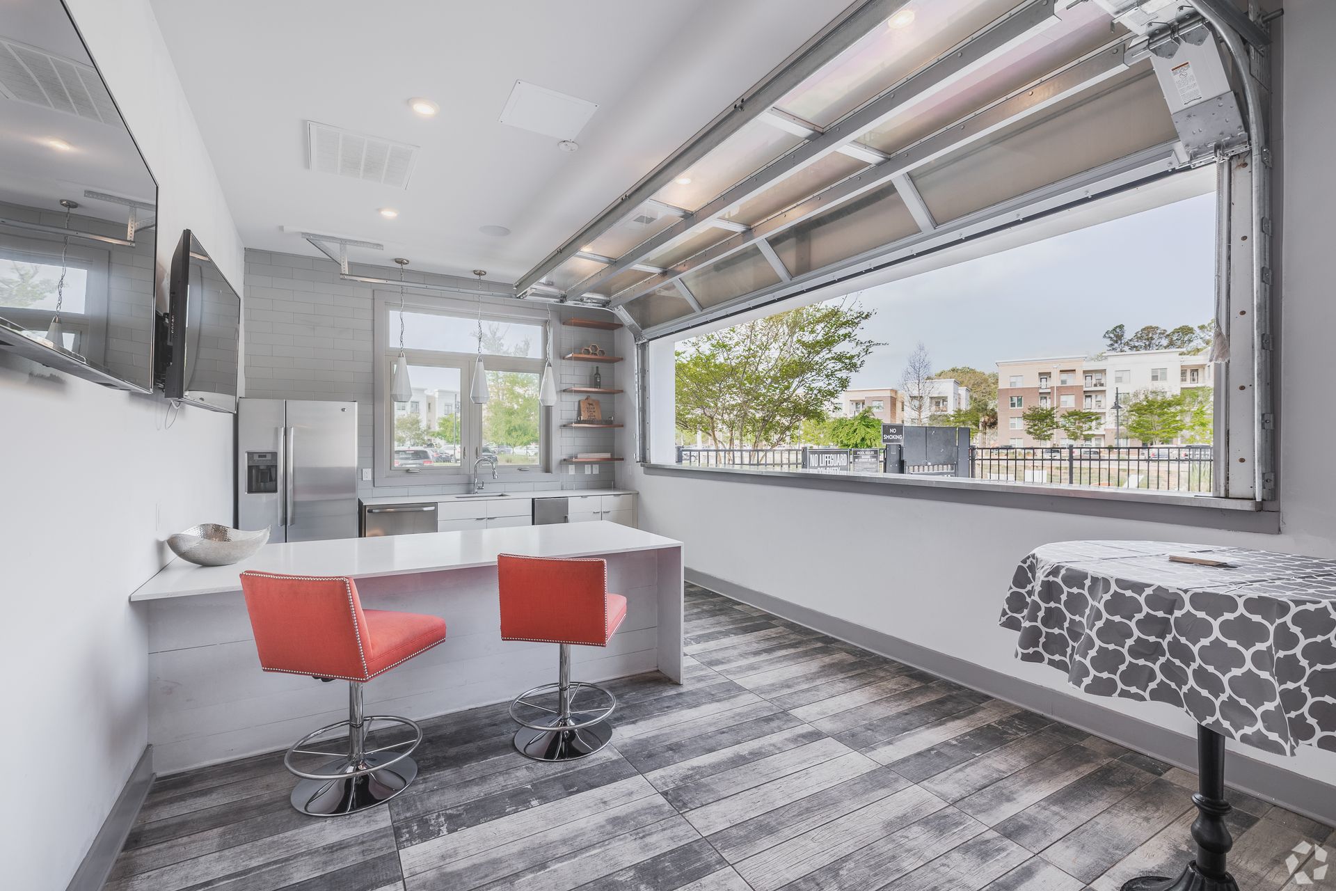 Bright modern office lounge with red stools, long white counter, and large windows overlooking trees