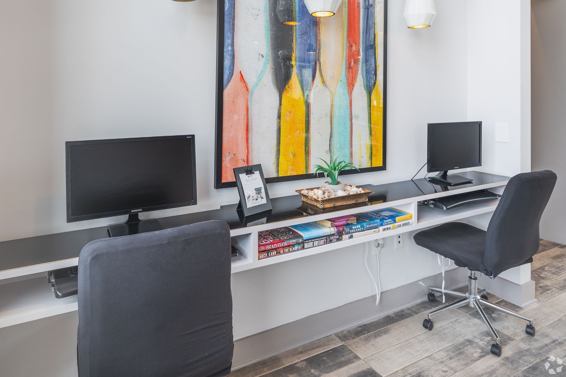 Modern office workspace with two computers, a long desk, and a colorful abstract wall painting