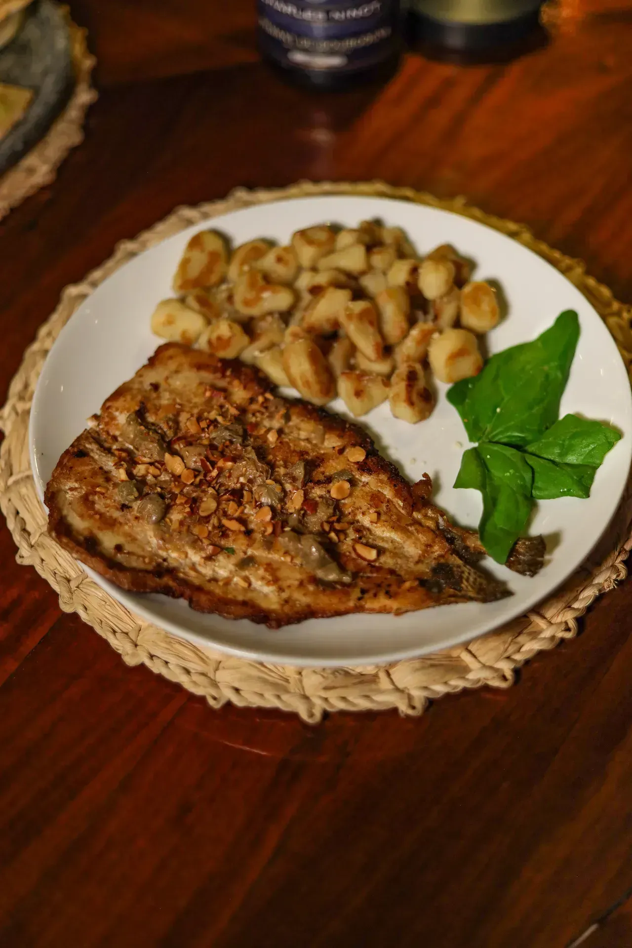 Filé de peixe grelhado com cogumelos e verduras salteados em um prato branco sobre uma mesa de madeira.