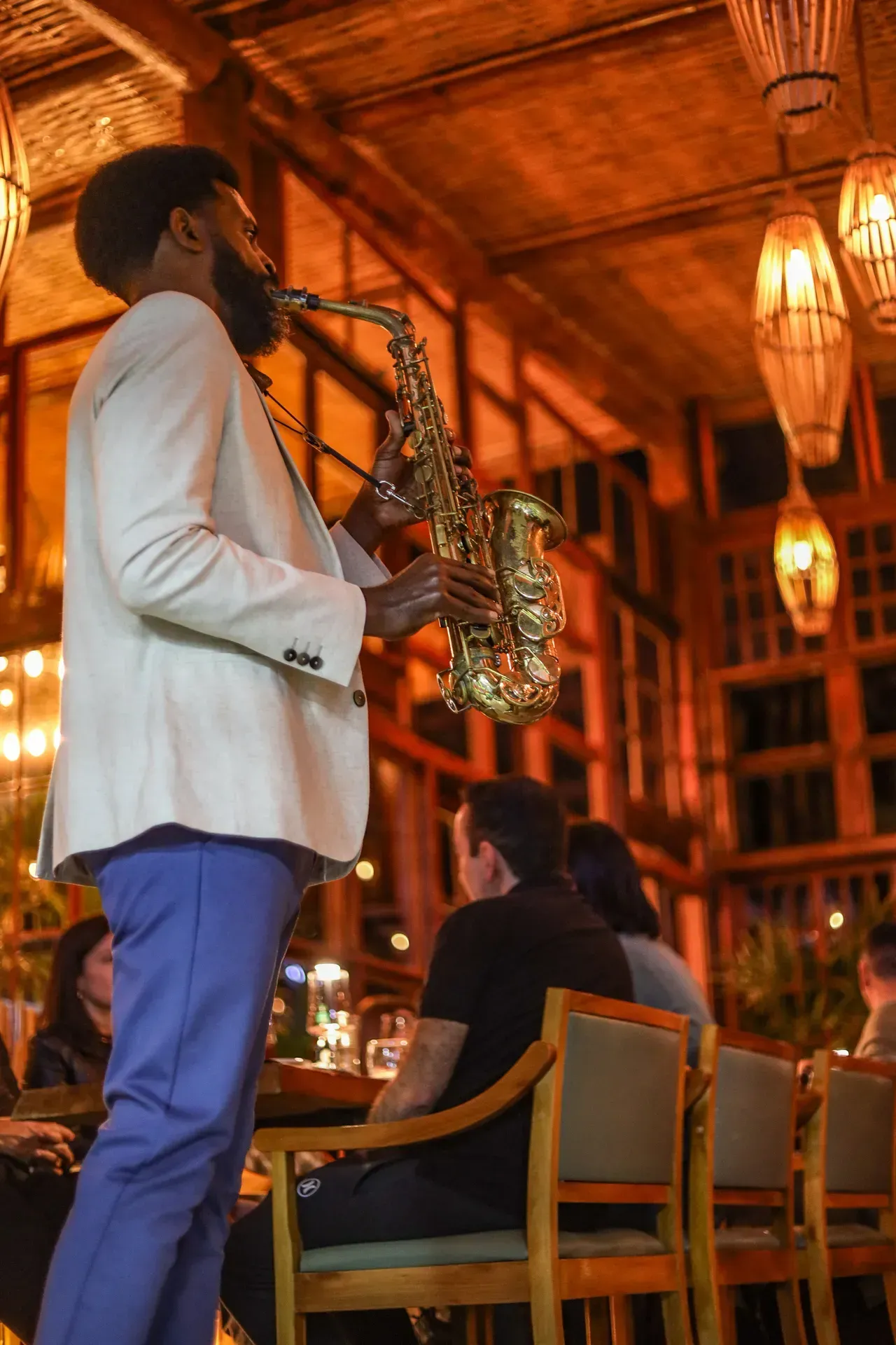 Saxofonista se apresentando em um restaurante com iluminação aconchegante, com clientes sentados por perto.