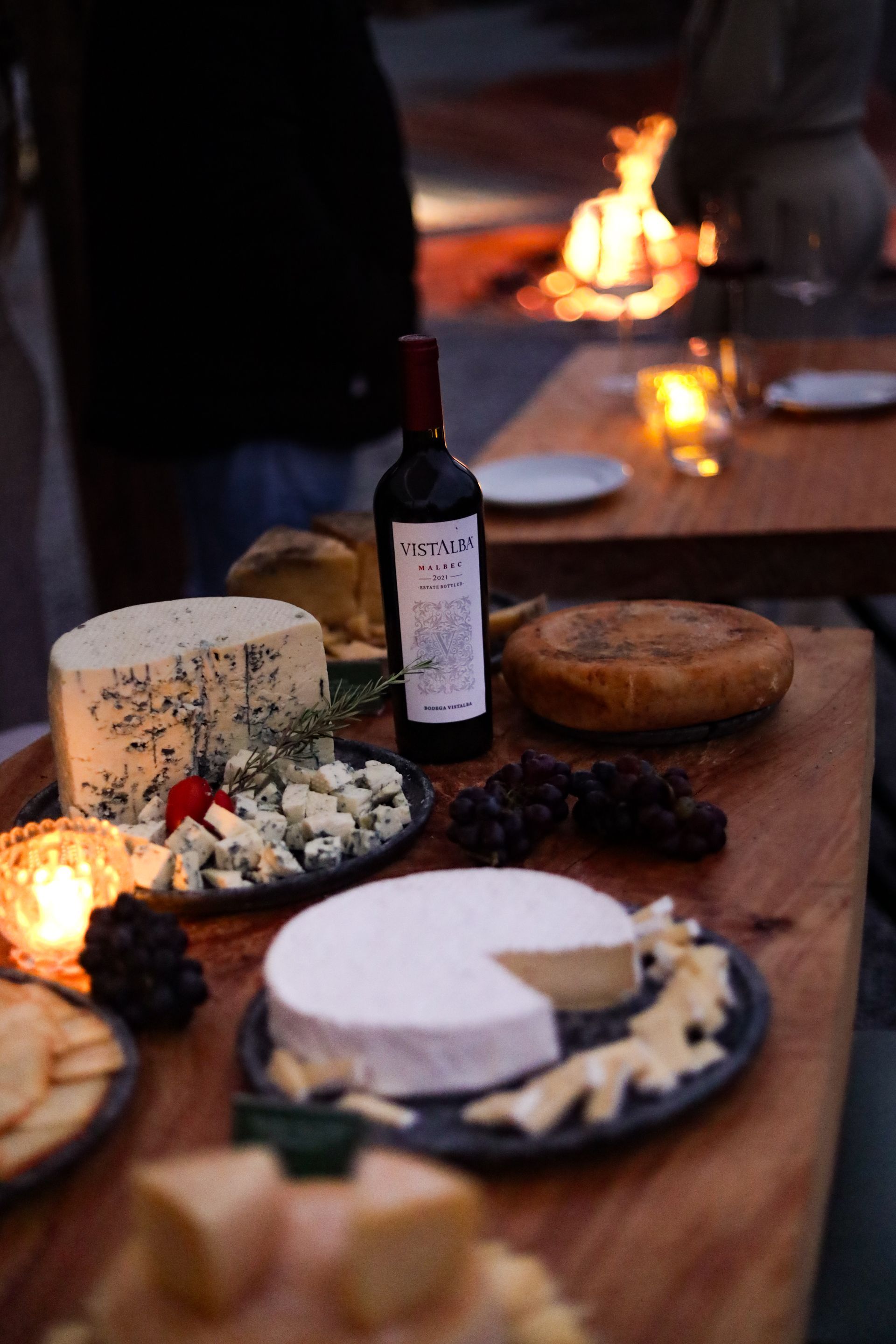 Garrafas de vinho e pratos de aperitivos sobre uma mesa em um restaurante ou sala de degustação com iluminação aconchegante.